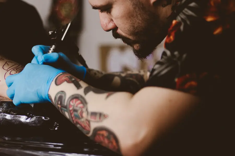 An artist in blue gloves working on a forearm sleeve.
